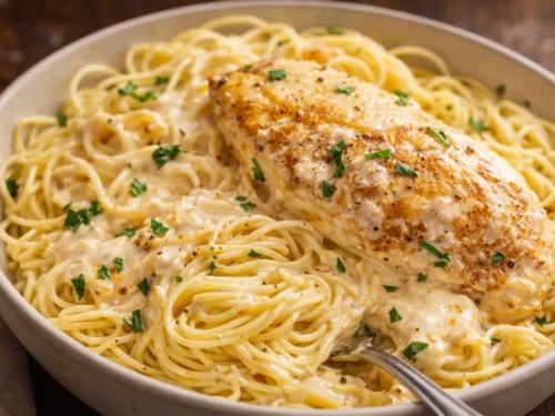 A White Plate Topped With Crockpot Angel Chicken And Creamy Sauce Over